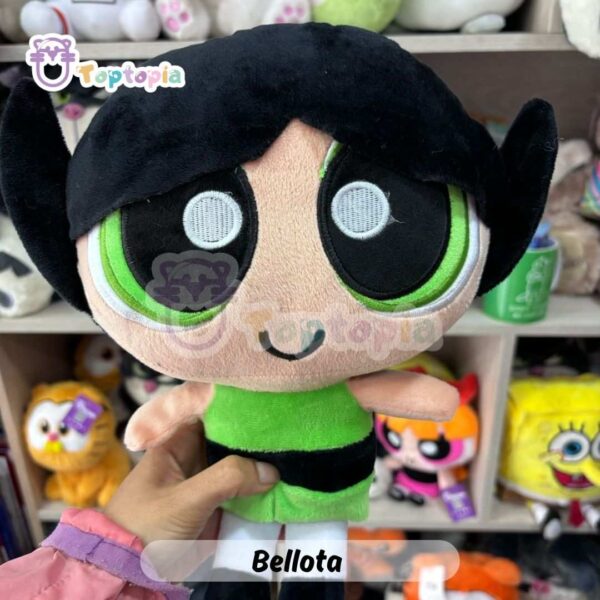 Peluche de Bellota, personaje de Las Chicas Superpoderosas, con cabello negro, vestido verde y mirada decidida, sobre fondo de tienda de juguetes.
