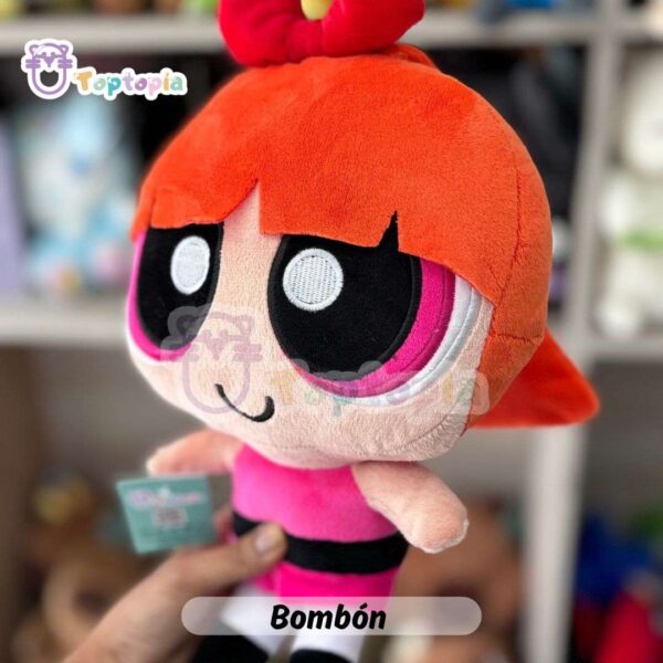 Peluche de Bombón, personaje de Las Chicas Superpoderosas, con vestido rosa y lazo rojo en la cabeza, sobre fondo de tienda de juguetes.
